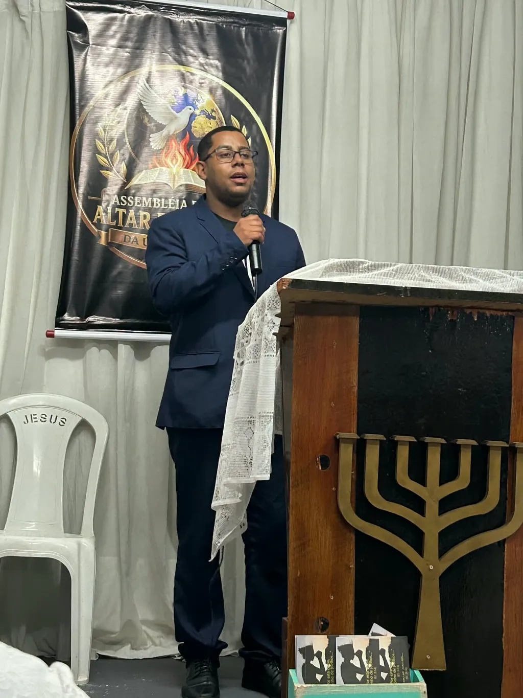 Pregação no púlpito, com o banner da igreja ao fundo